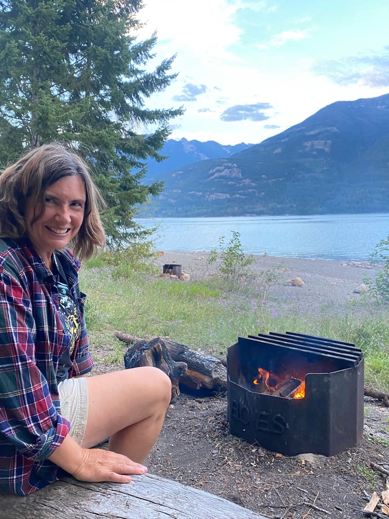 woman sitting lakeside enjoying campfire